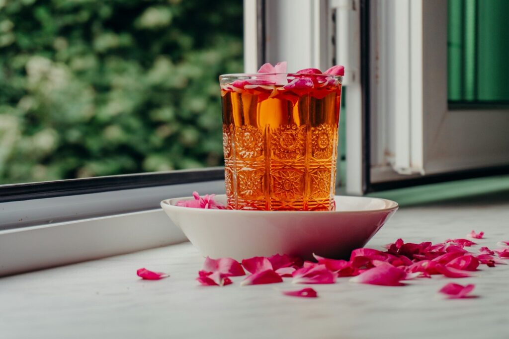 Glass of rose-infused drink with petals on a windowsill